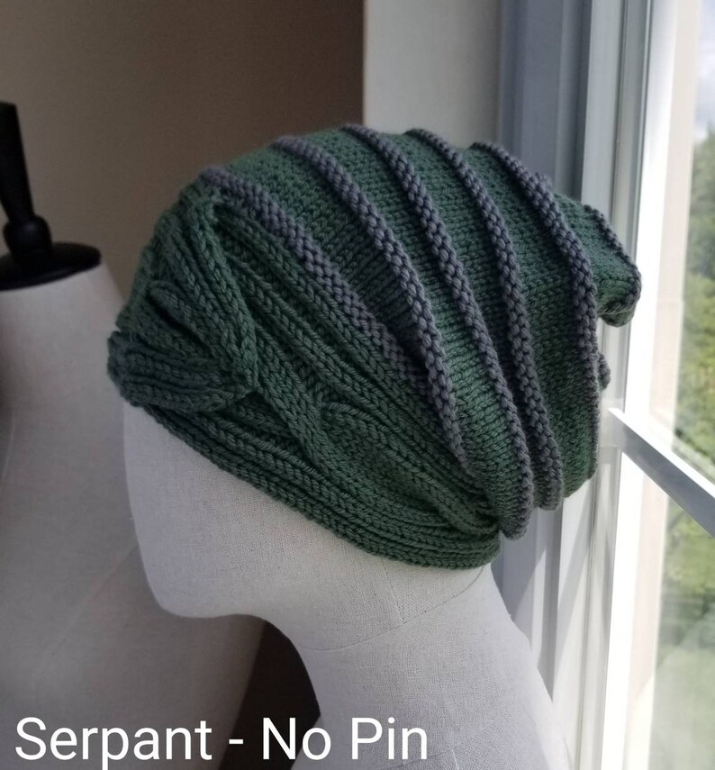 May include: A green and gray knitted beanie with a cable knit pattern. The beanie is on a white mannequin head. "Serpant - No Pin" is written below the mannequin.