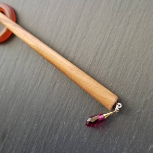 May include: A wooden hair stick with a dark brown finish and a small, teardrop-shaped, pink crystal pendant.