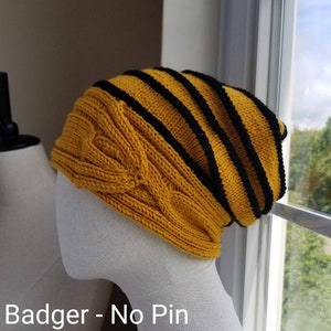 May include: A yellow and black striped knit beanie with a cable knit pattern. The beanie is on a white mannequin head. The text "Badger - No Pin" is visible below the beanie.