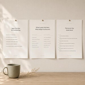 Può includere: Tre stampe rettangolari su carta color bianco sporco fissate a una parete, con testo nero intitolato Signs You May Be Overlooking, What Looks Like Rest, What Helps You Recover e The Seven-Day Quiet Reset, accompagnate da una tazza in ceramica grigio opaco.