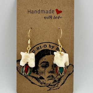 May include: Handmade earrings with bone-shaped pendants and gold-colored hooks. The pendants are paired with red and green beaded accents. The earrings are displayed on a brown card with the text "Handmade with love."