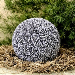 May include: A spherical decorative object featuring a dense, textured surface covered in numerous small, sculpted rose blossoms. The sculpture has a grey, weathered finish with darker shading in the crevices of the petals, creating a high-contrast look.