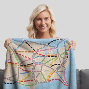 May include: A blue throw blanket with a map of the United States printed on it. The map shows the major cities and highways in the country. The blanket is being held by a person.