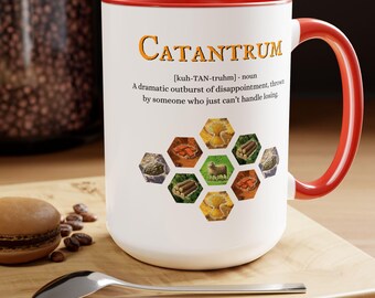 May include: White ceramic mug with a red rim and handle. The mug features a graphic of a hexagonal board game with a definition of the word "Catantrum" below it. The definition reads: "[kuh-TAN-truhm] - noun A dramatic outburst of disappointment, thrown by someone who just can't handle losing."