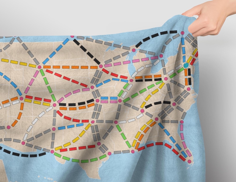 May include: A fabric map of the United States with a train route network printed on it. The map is in shades of blue, gray, white, black, red, orange, yellow, green, and pink.