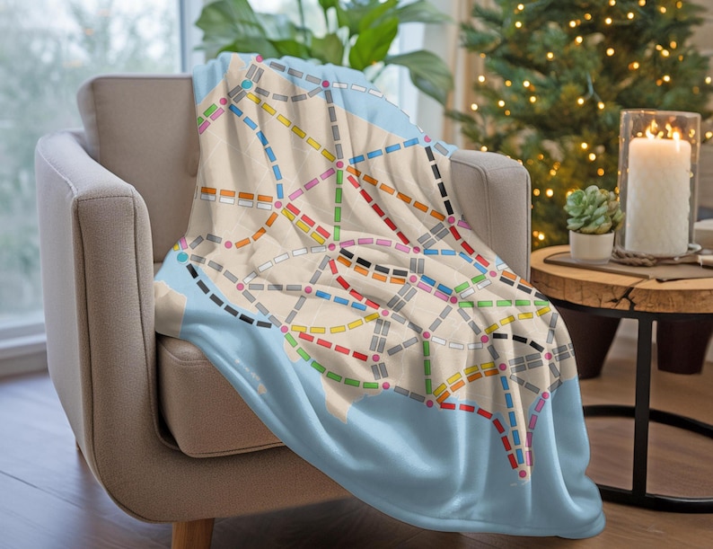 May include: A blue and white throw blanket with a colorful subway map design. The blanket is draped over a light brown armchair.
