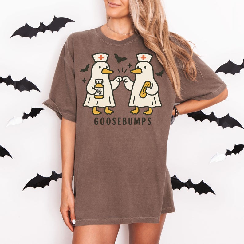 May include: Brown t-shirt with a graphic of two cartoon ducks wearing nurse hats and holding medical items. The text "GOOSEBUMPS" is printed below the ducks. Black bat cutouts decorate the background.