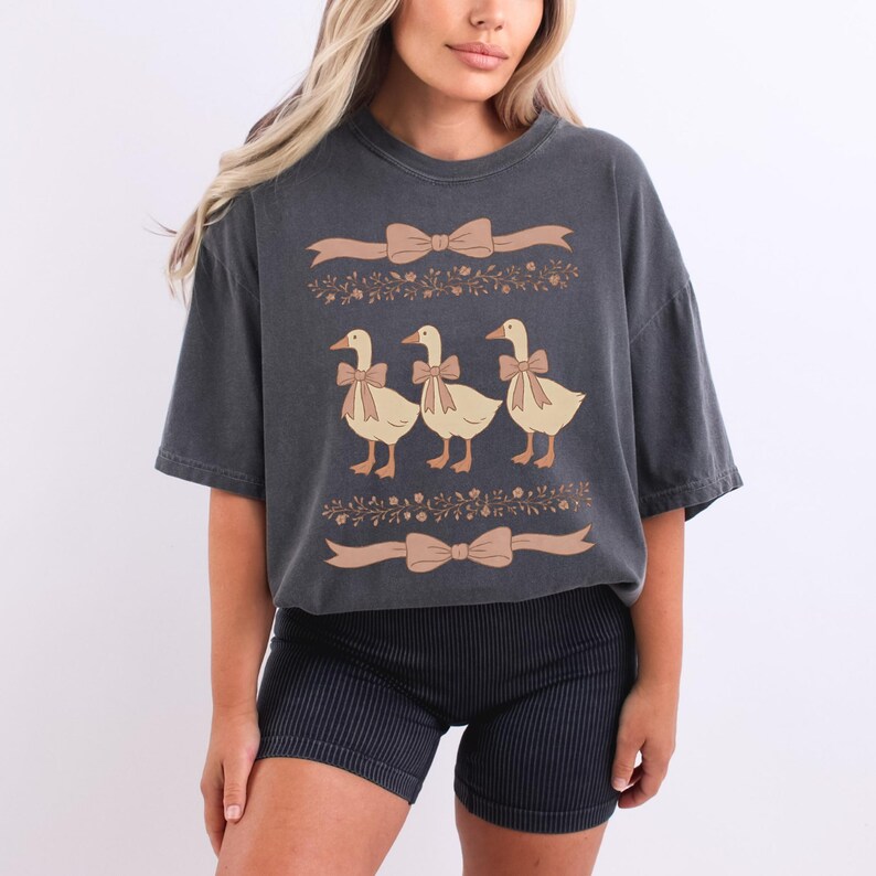 May include: A dark gray oversized t-shirt with a graphic of three ducks in a row wearing bows. The ducks are surrounded by floral designs and bows.