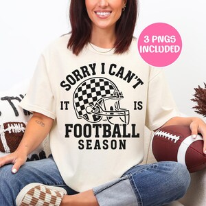 K&ouml;nnte beinhalten: Cremefarbenes T-Shirt mit dem schwarzen Text "SORRY I CAN'T IT IS FOOTBALL SEASON". Das Design beinhaltet einen Footballhelm mit Schachbrettmuster. Ein rosa Kreis mit "3 PNGS INCLUDED" befindet sich oben rechts.