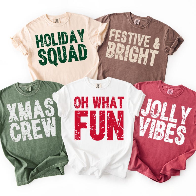 May include: Five t-shirts in various colors, each with a different holiday-themed phrase in bold, distressed lettering. Phrases include "Holiday Squad," "Festive & Bright," "Xmas Crew," "Oh What Fun," and "Jolly Vibes."