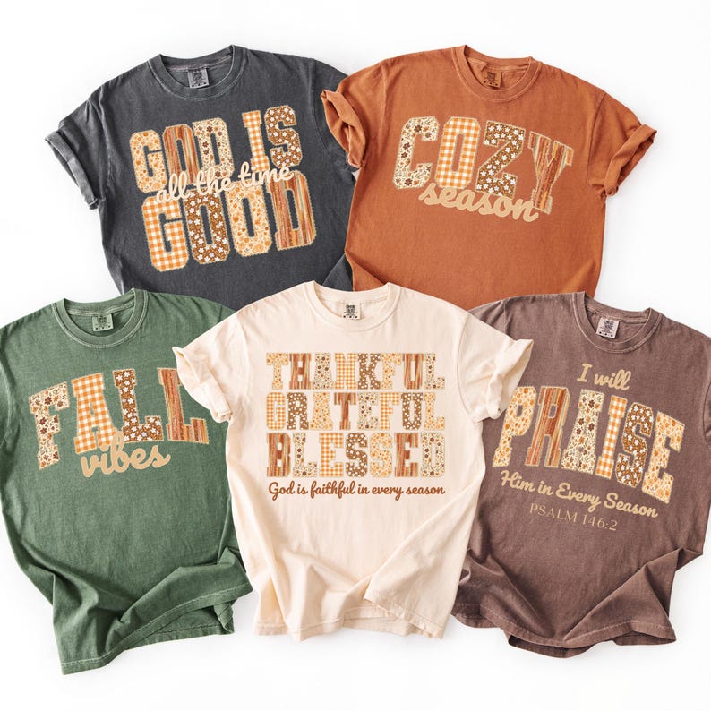 May include: Five t-shirts with fall-themed graphics. The shirts are in various colors, including gray, orange, green, cream, and brown. Each shirt features a different phrase, such as "God is Good," "Cozy Season," and "Fall Vibes," in a decorative font.