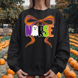 May include: Black sweatshirt with a Halloween-themed design. The design features the word "NURSE" in purple, white, black, green, and orange, with a ghost replacing the "U". An orange and purple bow is above the word.