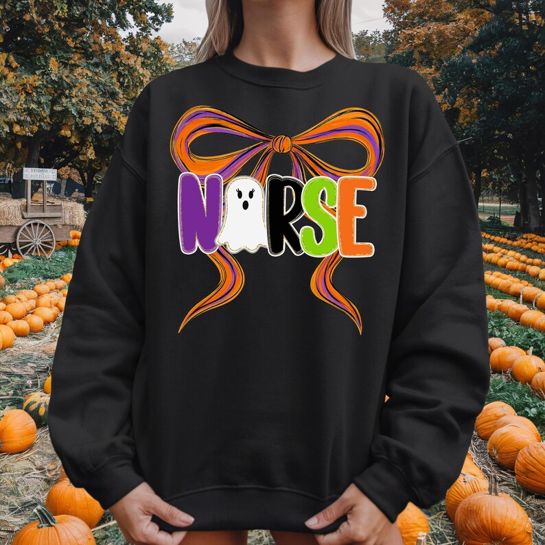 May include: Black sweatshirt with a Halloween-themed design. The design features the word "NURSE" in purple, white, black, green, and orange, with a ghost replacing the "U". An orange and purple bow is above the word.