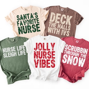 May include: Five t-shirts with holiday-themed phrases for nurses. The shirts are in various colors, including beige, brown, green, white, and red. Text includes "Santa's Favorite Nurse," "Deck the Halls with IVs," "Nurse Life Sleigh Life," "Jolly Nurse Vibes," and "Scrubbin' Through the Snow."