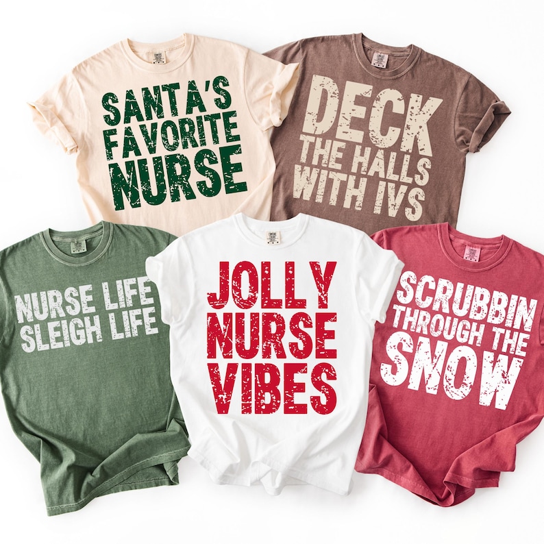 May include: Five t-shirts with holiday-themed phrases for nurses. The shirts are in various colors, including beige, brown, green, white, and red. Text includes "Santa's Favorite Nurse," "Deck the Halls with IVs," "Nurse Life Sleigh Life," "Jolly Nurse Vibes," and "Scrubbin' Through the Snow."