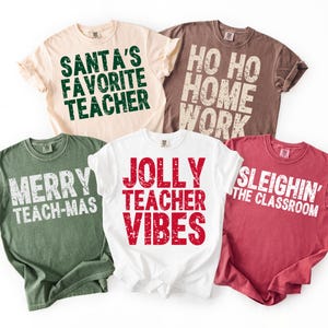 May include: Five t-shirts in various colors, each with a holiday-themed message for teachers. The shirts are beige, brown, white, green, and red. Text includes "Santa's Favorite Teacher," "Ho Ho Home Work," and "Jolly Teacher Vibes."