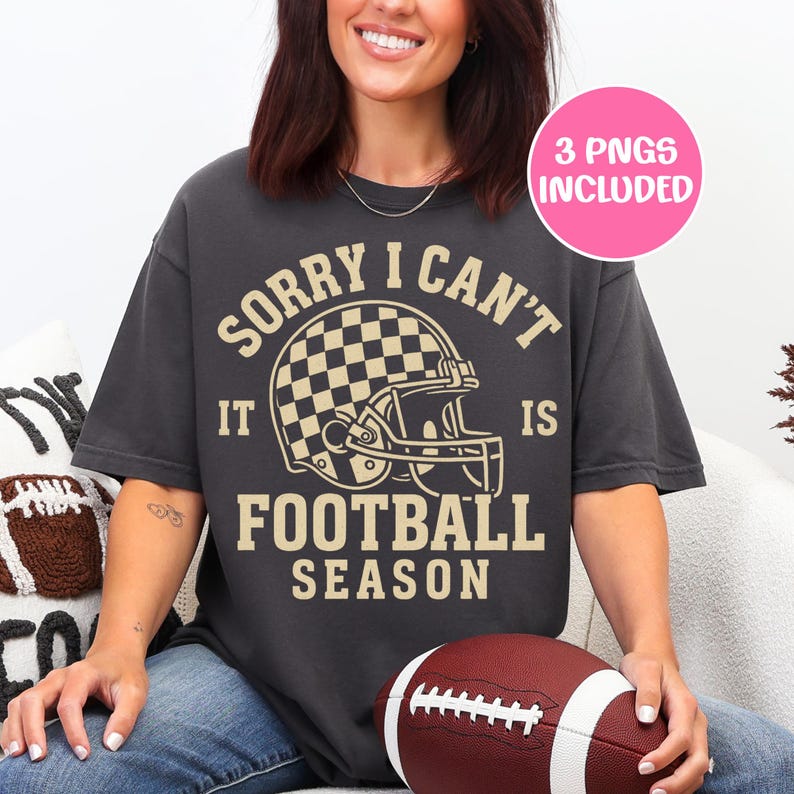K&ouml;nnte beinhalten: Dunkelgraues T-Shirt mit dem Text "SORRY I CAN'T IT IS FOOTBALL SEASON" und einer Footballhelm-Grafik. Ein rosa Kreis oben rechts zeigt "3 PNGS INCLUDED". Ein Football wird im Scho&szlig; gehalten.