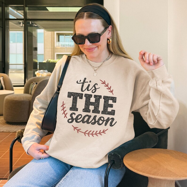 May include: A beige sweatshirt with a black and red graphic that says "'tis THE season" in a circle with red stitching around it.