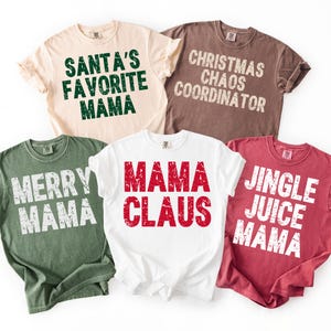 May include: Five short-sleeved t-shirts in various colors, each with a holiday-themed phrase. The shirts are beige, brown, white, green, and red. Phrases include "Santa's Favorite Mama," "Christmas Chaos Coordinator," and "Jingle Juice Mama."