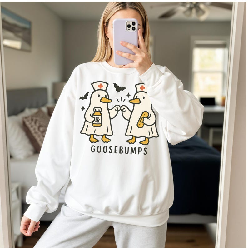 May include: White sweatshirt featuring a cartoon design of two ducks dressed as medical professionals. One duck holds a prescription bottle, the other a bandage. The word "GOOSEBUMPS" is printed below the ducks. Black bat silhouettes are above the ducks.