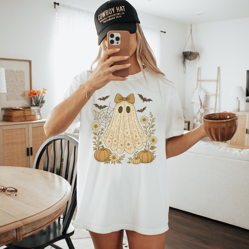 Puede incluir: Camiseta blanca con un dise&ntilde;o de fantasma vintage, con un lazo, calabazas, flores y murci&eacute;lagos. El fantasma tiene una apariencia de encaje. La camiseta es de estilo casual y c&oacute;modo.