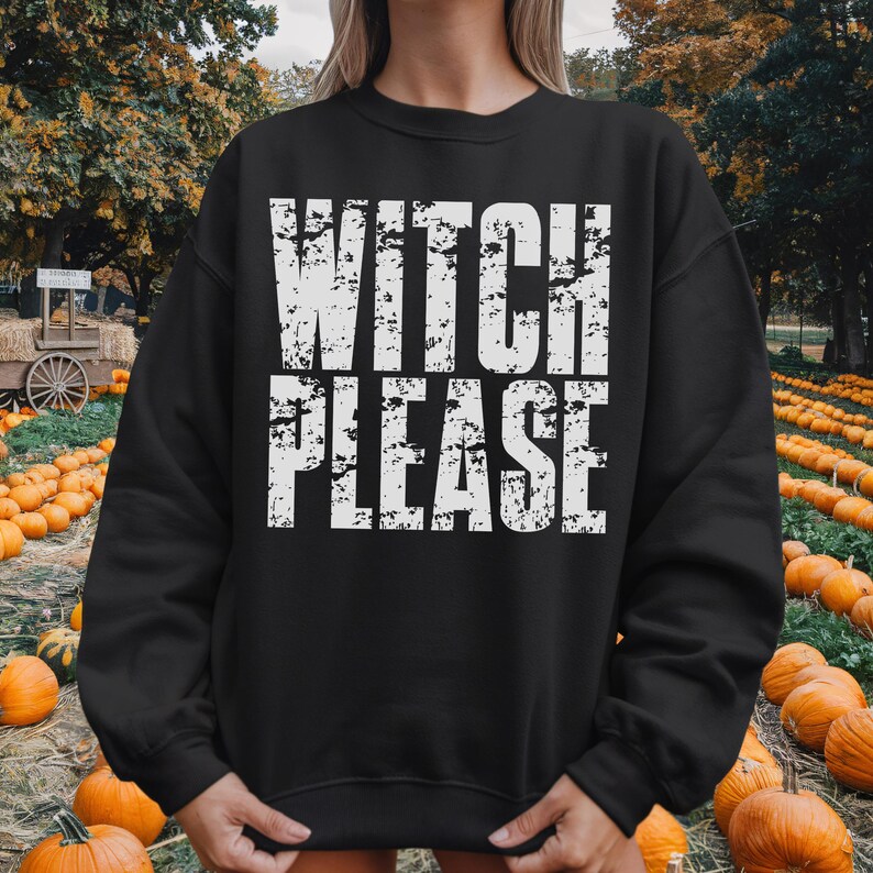 May include: Black sweatshirt with the text "WITCH PLEASE" in distressed white lettering. The sweatshirt is a crew neck style. The background shows a pumpkin patch with pumpkins and trees.
