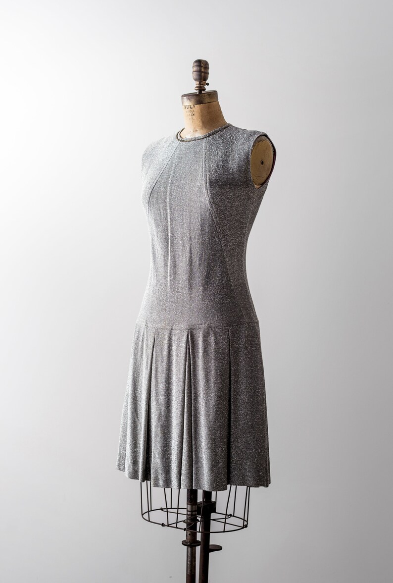 May include: A silver and gray sleeveless dress with a pleated skirt on a dress form.