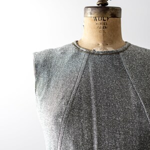 May include: A silver sleeveless dress with a textured fabric. The dress is on a vintage dress form with the text "WOLF MODEL FORM CO."