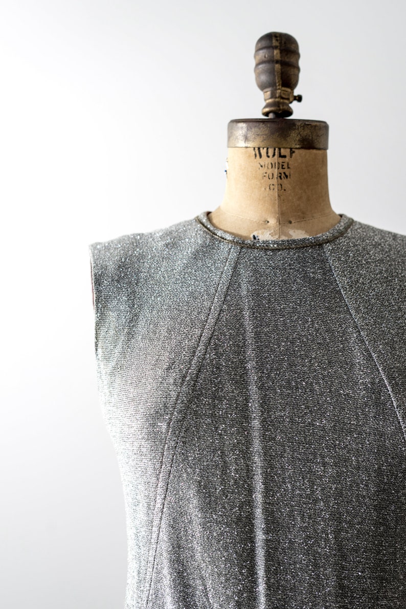 May include: A silver sleeveless dress with a textured fabric. The dress is on a vintage dress form with the text "WOLF MODEL FORM CO."