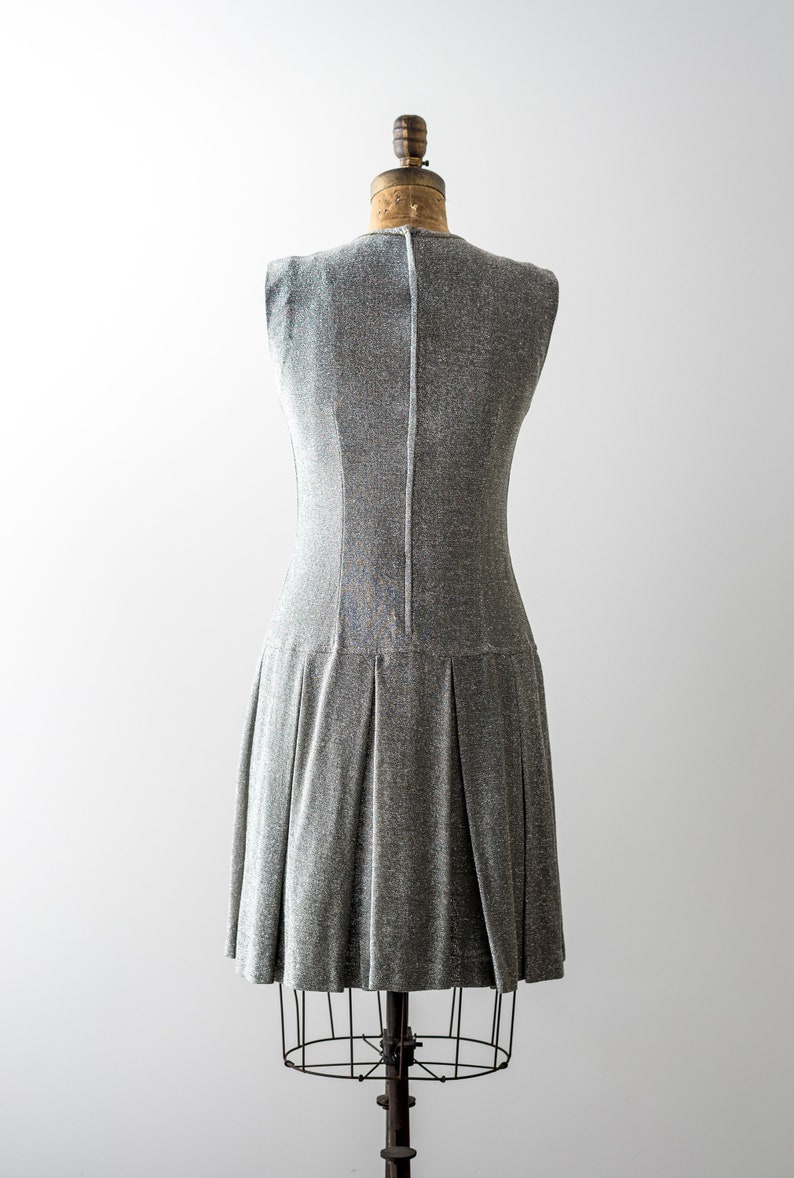 May include: A silver sleeveless dress with a pleated skirt on a dress form.