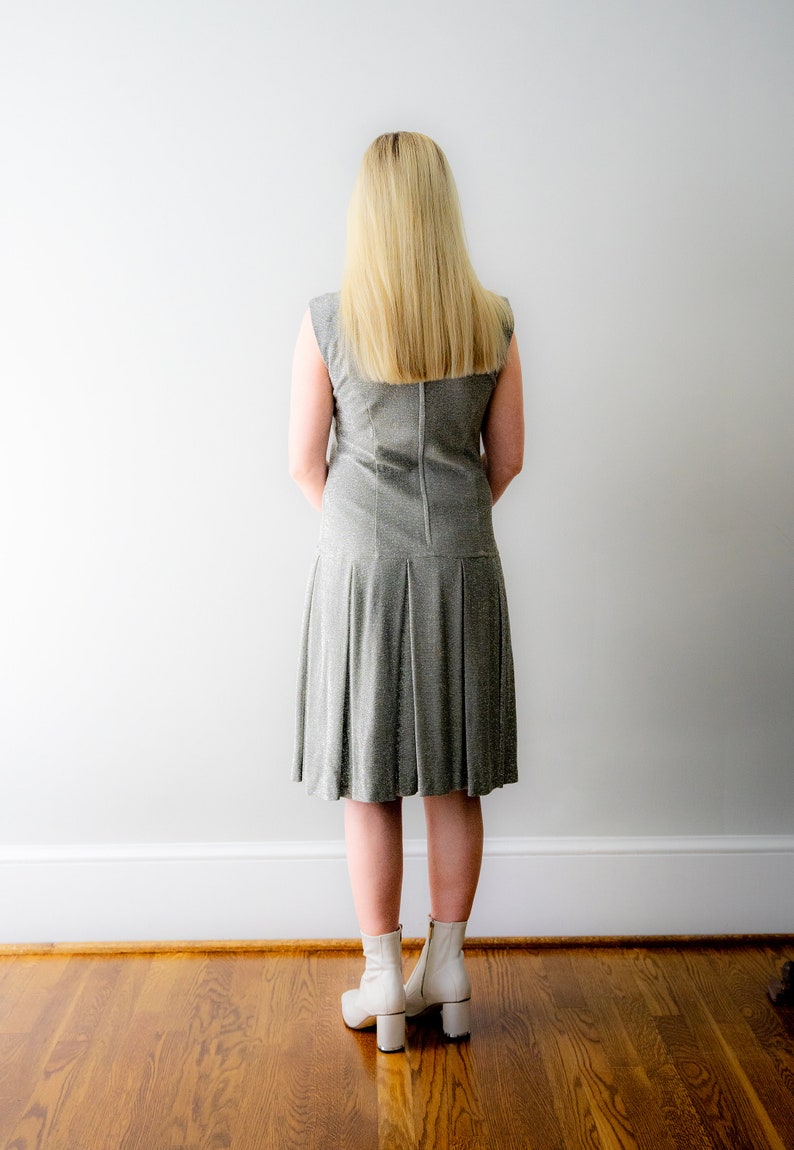 May include: A woman wearing a silver sequined dress with a pleated skirt and white ankle boots.