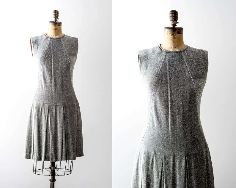 May include: A sleeveless gray dress with a pleated skirt. The dress is on a mannequin.