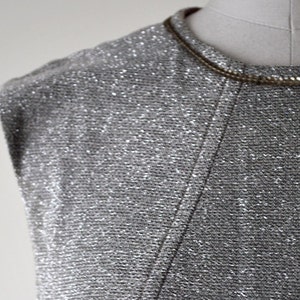 May include: A silver sleeveless top with a sparkly texture. The top has a scoop neck and a simple design.