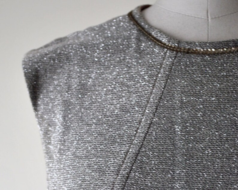 May include: A silver sleeveless top with a sparkly texture. The top has a scoop neck and a simple design.