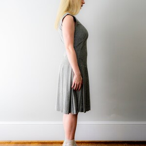 May include: A woman wearing a gray, sleeveless dress with a slightly flared skirt. She is wearing white ankle boots with a block heel.