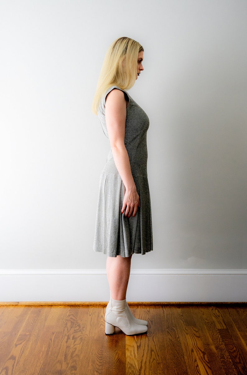May include: A woman wearing a gray, sleeveless dress with a slightly flared skirt. She is wearing white ankle boots with a block heel.