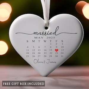 May include: White heart-shaped ornament with the word "married" and a calendar for May 2025. The date May 16th is highlighted in red. The names "Oliva & James" are written below the calendar. A white ribbon is attached for hanging.