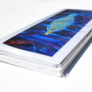 May include: A stack of white cards with a colorful image of a fish swimming in a blue and purple coral reef. The image is printed on the front of the cards.