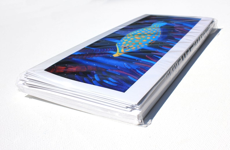 May include: A stack of white cards with a colorful image of a fish swimming in a blue and purple coral reef. The image is printed on the front of the cards.