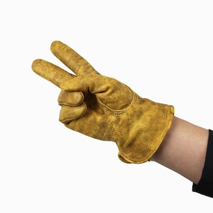 May include: A close-up of a tan work glove, showing the index and middle fingers extended in a peace sign. The glove is made of a textured material, and the wrist is visible with a black sleeve.