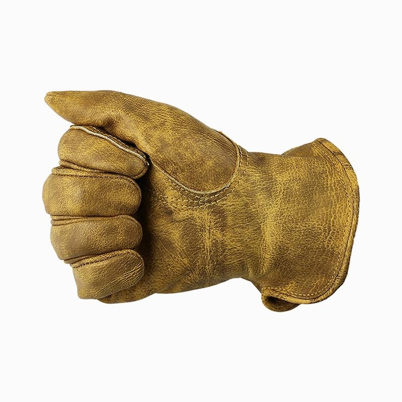 May include: A close-up of a work glove made of distressed, tan-colored leather. The glove is worn and shows signs of use, with visible stitching and a reinforced palm. The fingers are slightly curved, suggesting it is in use.