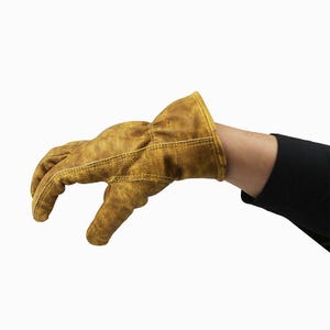 May include: A tan leather work glove with a distressed finish. The glove is worn on a person's hand, with the fingers slightly curved. The cuff is a darker shade of tan, and the glove appears to be well-worn.