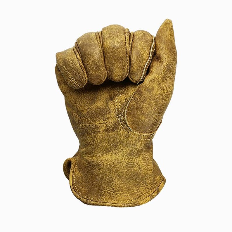 May include: A close-up of a work glove made of distressed brown leather. The glove is clenched into a fist, showcasing the stitching and texture of the material. The glove appears worn, suggesting durability and use.