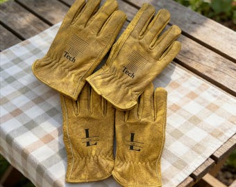 Puede incluir: Cuatro pares de guantes de trabajo de cuero color canela están colocados sobre una tela a cuadros. Dos pares tienen la palabra "Tech" impresa, y los otros dos la letra "L". Los guantes están sobre una mesa de madera.