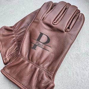 May include: A pair of brown leather gloves with the name "Paul" printed in black. The gloves are made of a soft, supple leather and have a classic design, perfect for gardening or outdoor work.