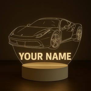 May include: A glowing LED night light featuring a sports car outline with the text "YOUR NAME" in a bold font. The light has a beige base and a clear acrylic top with the car design.