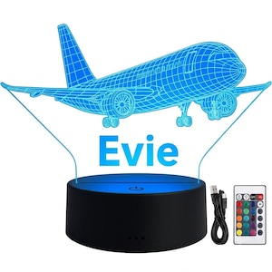 Puede incluir: Una lámpara de ilusión 3D con un gráfico de avión en estructura de alambre azul y el nombre Evie en texto azul. La lámpara se asienta sobre una base circular negra con un botón de encendido. Incluye un cable USB negro y un mando a distancia.