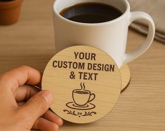 May include: A light wood coaster with the text "YOUR CUSTOM DESIGN & TEXT" and a coffee cup graphic. A white mug filled with coffee sits behind the coaster. The coaster is round and has a wood grain pattern.