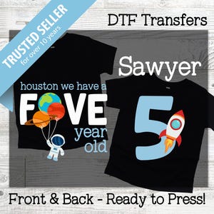 Peut inclure: Deux t-shirts noirs avec des motifs sur le thème de l'espace. L'un dit "houston we have a FIVE year old" avec des planètes et un astronaute. L'autre porte le nom "Sawyer" et un grand chiffre "5" avec une fusée.