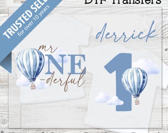 May include: White t-shirt transfers with hot air balloon designs. One design says "mr ONE -derful" with a blue and white balloon. Another design has the name "derrick" and a number "1" with a balloon. The text "DTF Transfers" is at the top.